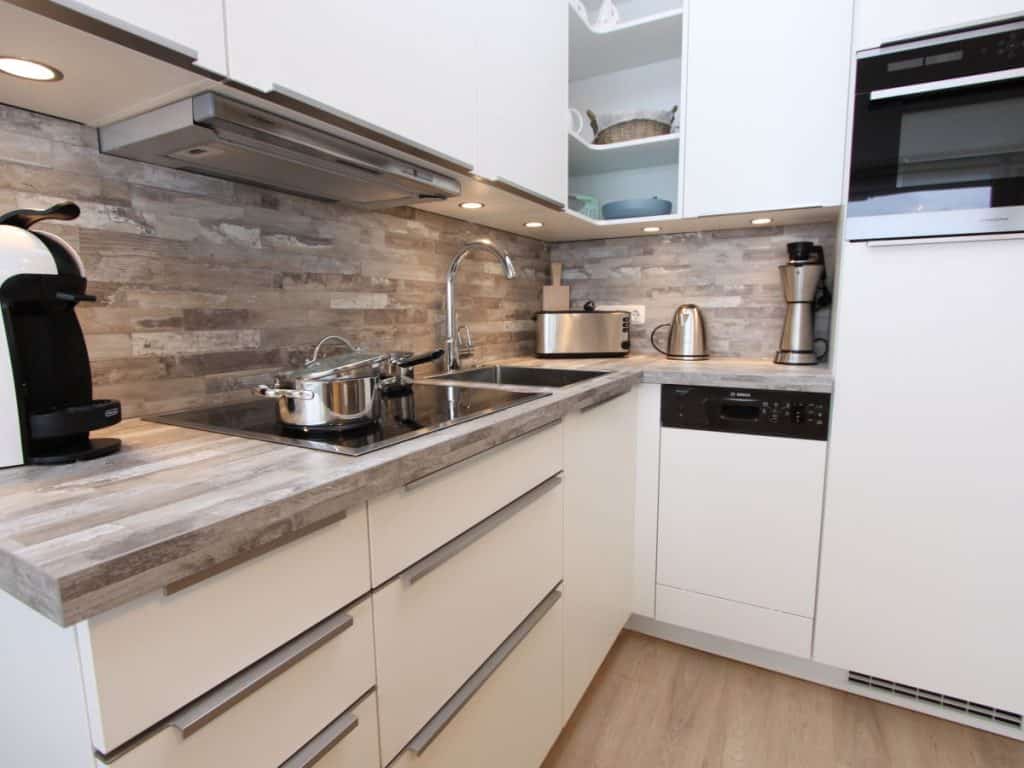 Moderne Einbauküche mit Geschirrspüler ist in das Wohnzimmer integriert und mit hochwertigem Inventar versehen.